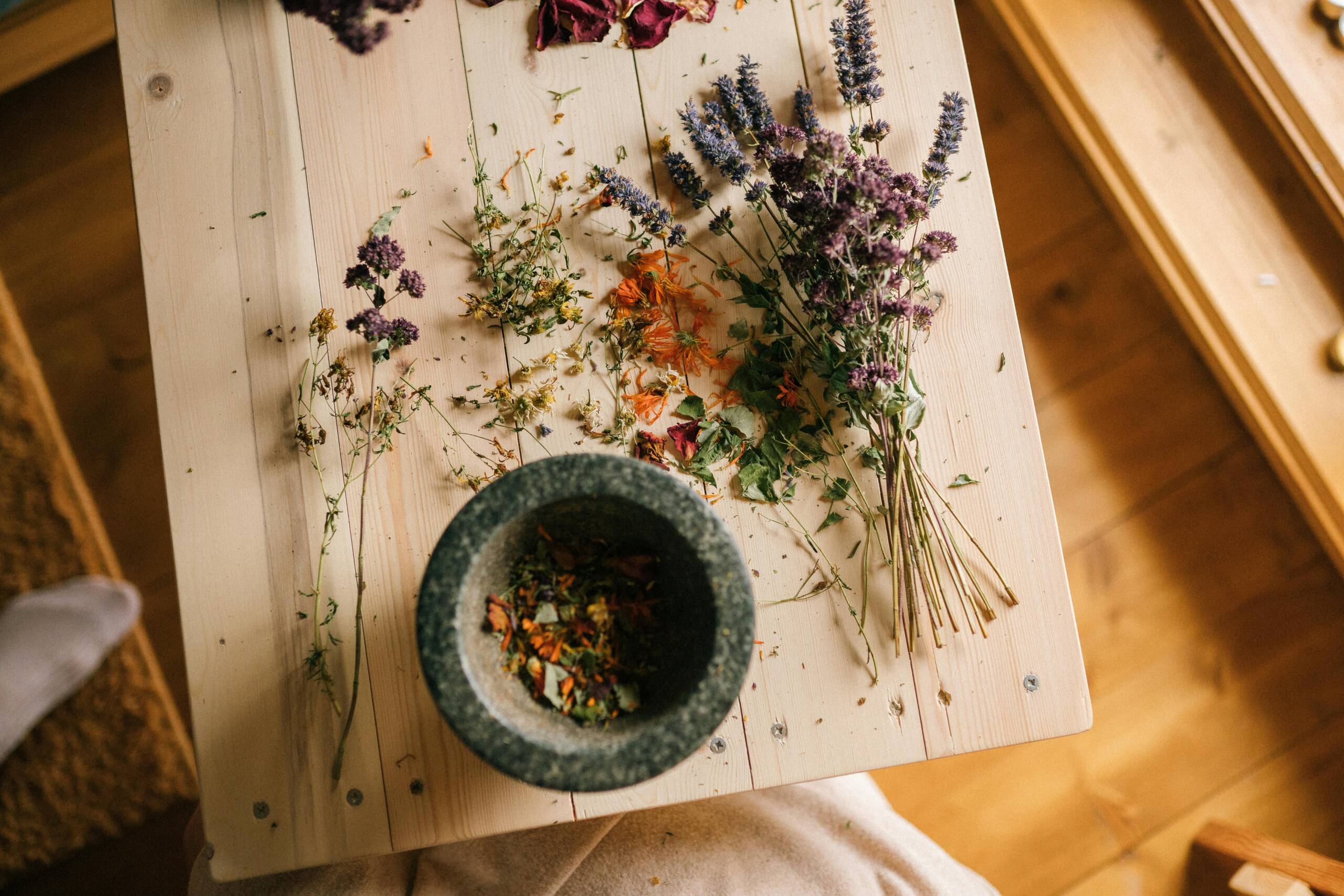 Dried herbs and flowers arranged on a wooden table with a stone mortar for home remedies.