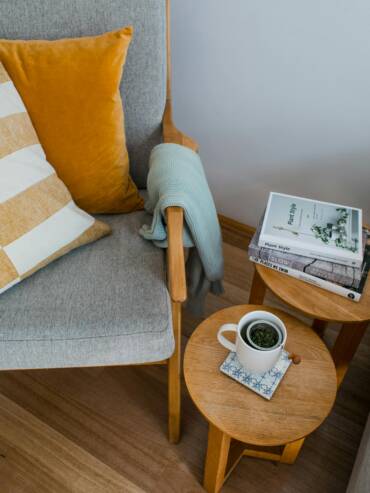 Holistic well-woman care in a cozy, trauma-informed setting. From above of comfortable armchair with colorful pillows placed near wooden side tables with books and cup of tea in living room. 
